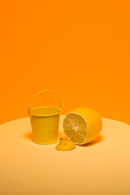 Abstract still life with a yellow bucket and a lemon on an orange