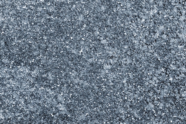 Abstract texture of the frozen asphalt of dark blue color with snow grains for a natural background