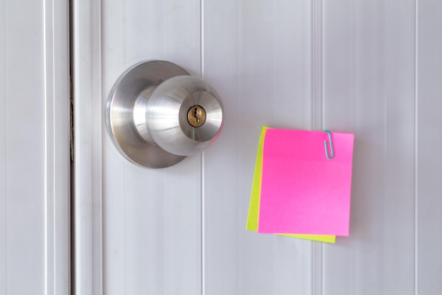 Abstract white door with metal doorknob is lock and sticker\
paper note on door text paper reminds the door for message