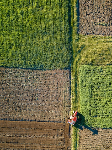 Abstracte geometrische vormen van landbouwvelden met verschillende gewassen en grond zonder inzaaien van gewassen, gescheiden door weg en tractor erop, in groene en zwarte kleuren. Een vogelperspectief vanaf de drone.