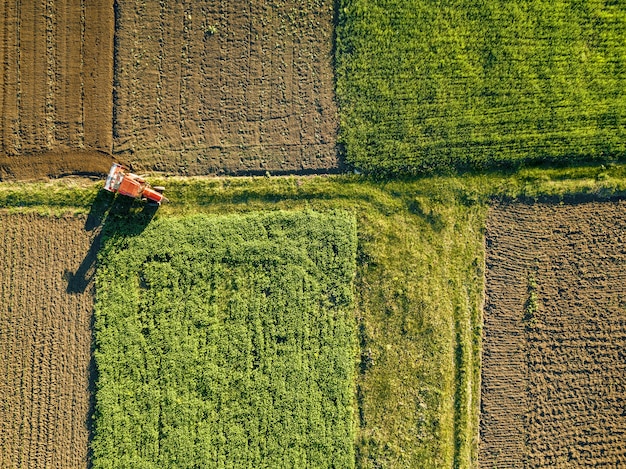 Abstracte geometrische vormen van landbouwvelden met verschillende gewassen en grond zonder inzaaien van gewassen, gescheiden door weg en tractor erop, in groene en zwarte kleuren.