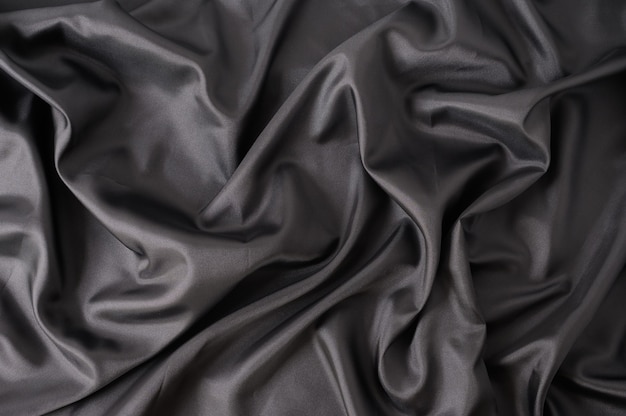 Abstracte zwarte satijnen zijdeachtige doek. Stof Textiel Drape met Plooi Golvende Vouwen achtergrond. Met zachte golven en, wuivend in de wind Textuur van verfrommeld papier.