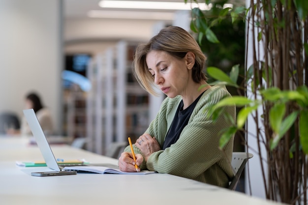 Academic career female university professor taking notes in day planner while sitting in library