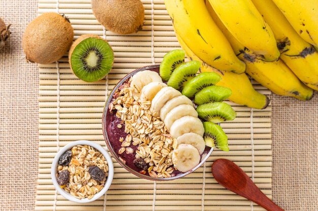 Acai, Close up on Brazilian acai bowl with banana, kiwi and oat flakes on bamboo placemat, top view.