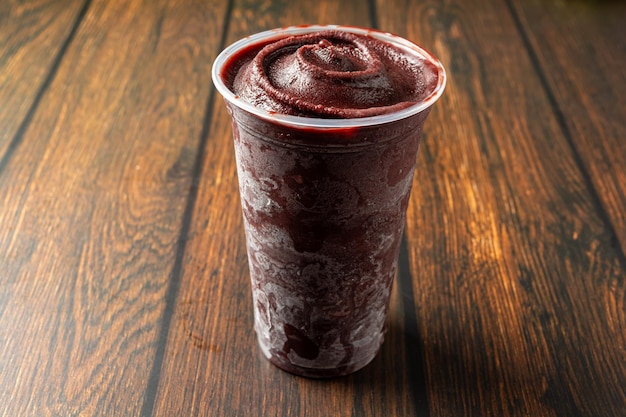 Acai in a plastic cup over wooden table ready for delivery