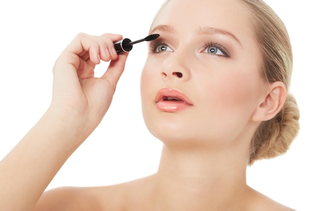 Accentuating her eyelashes a gorgeous young woman applying mascara while isolated on white