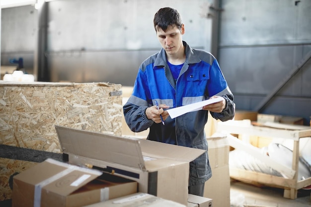 Acceptance of goods in the warehouse A young worker in overalls checks the goods according to the inventory