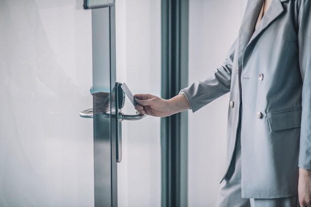 Система доступа. Рука женщины в сером деловом костюме, открывающая дверь офиса с пропускной картой