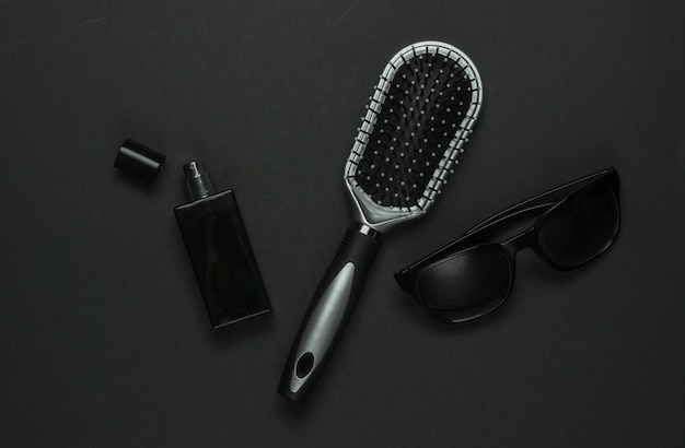 Accessoires voor dames op een zwarte achtergrond. Zonnebril, parfumflesje, kam. Bovenaanzicht