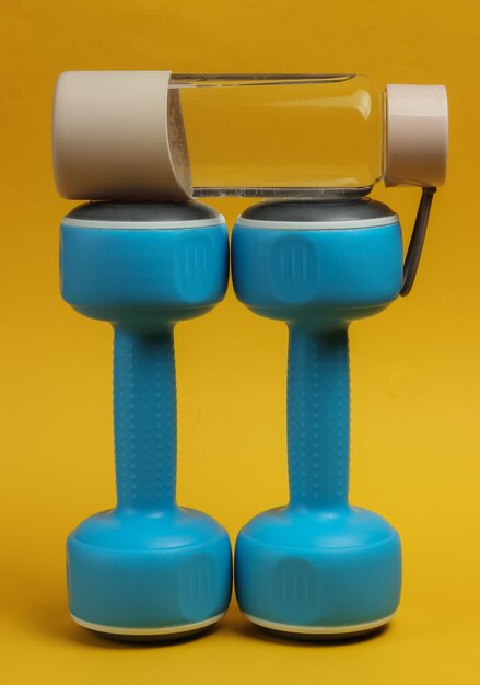 Accessoires voor fitness en sport op gele achtergrond. Halters, fles water.