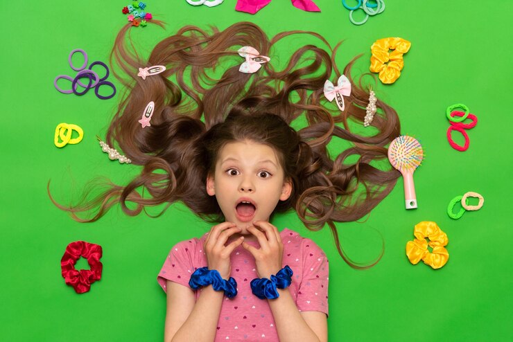 Accessoires voor kinderkapsels Een tiener met los krullend haar Een klein meisje met elastische banden en haarclips ligt en is verrast met haar mond wijd open op een groene geïsoleerde achtergrond
