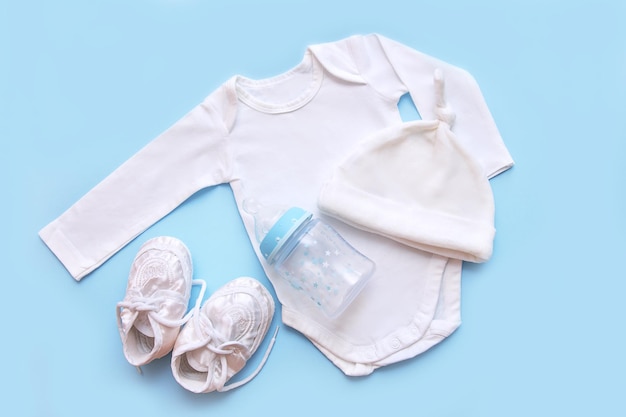 Accessories for a newborn on a blue background cap bodysuit booties milk bottle