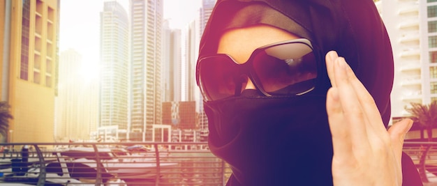 accessory, fashion and people concept - close up of muslim woman in hijab and sunglasses over dubai city street background