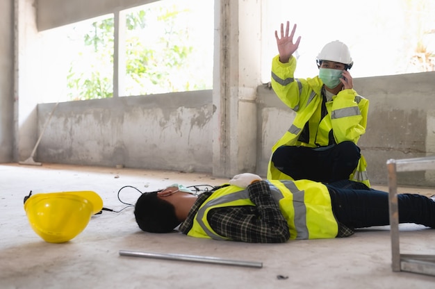 Photo an accident of a man worker at the construction site and call to the safety officer for rescue and life-saving. selection focus on an injured person.