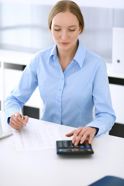 会計士は財務諸表をチェックするか、税務フォームの電卓収入で数えます。オフィスの机に座って働くビジネスウーマン監査の概念