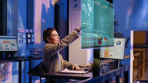 accountant imputing revenue figures on computer in office during nightshift, visualizing them using augmented reality. employee at desk focused on typing company statistical numbers, working overnight