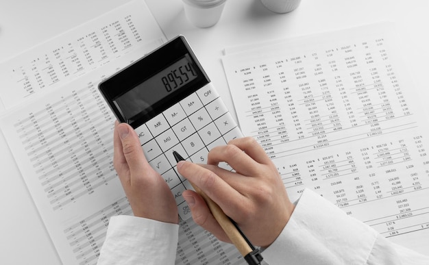 財務諸表と白い背景のデスク オフィスで電卓を使用する会計士トップ ビュー