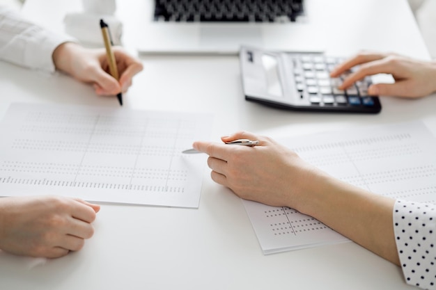 Photo accountant using a calculator and laptop computer for counting taxes with a client or a colleague at white desk in office teamwork in business audit and finance