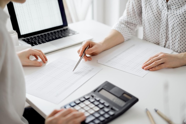 Photo accountant using a calculator and laptop computer for counting taxes with a client or a colleague at white desk in office teamwork in business audit and finance