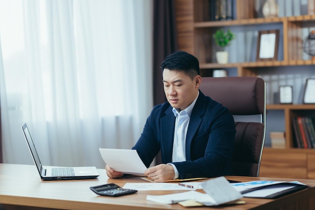 Photo accountantauditor works in a classic office calculates financial reports asian businessman works with computer and documents paperwork