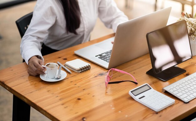 Foto donna contabile che usa un computer portatile sul tavolo del posto di lavoro con tablet digitale e calcolatrice al caffè