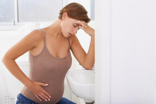 The aches and pains of pregnancy A pregnant woman struggling with morning sickness in the bathroom