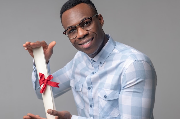 Achievement, pleasure. happy successful dark skinned man with\
glasses holding important scroll in his hands in excellent\
mood