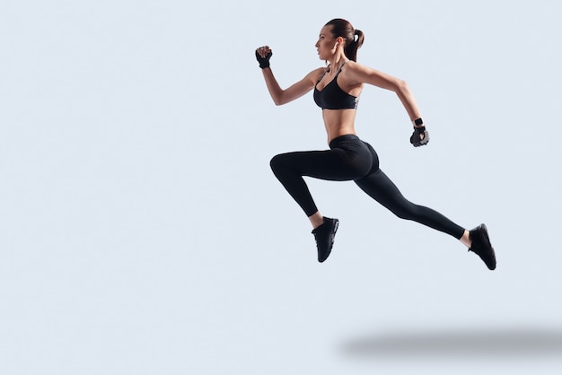 Achieving best results. Full length of attractive young woman in sports clothing exercising while hovering against grey background