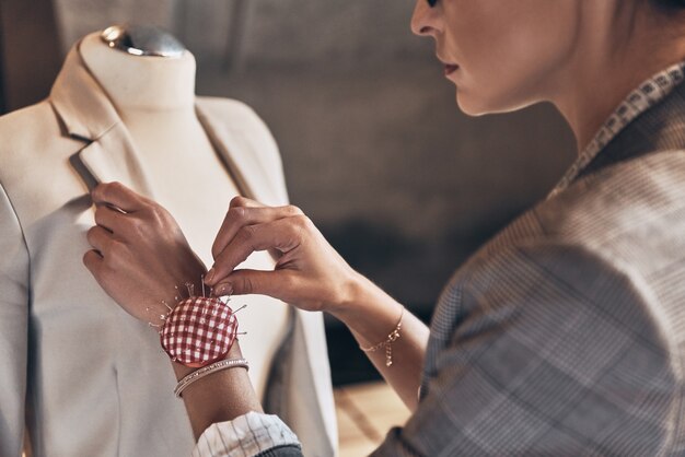 Achieving success as a designer. Close up rear view of young woman using sewing needles while standing in her workshop