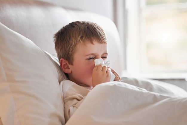 Achooo Shot of a little boy feeling ill in bed at home and blowing his nose