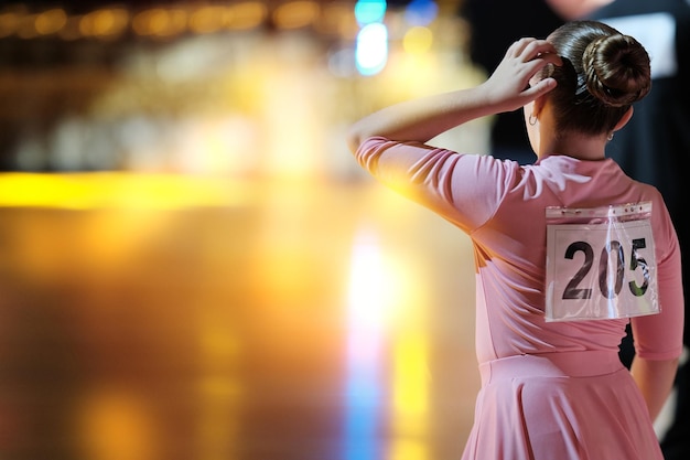 Foto achter de danseres een meisje dansatleet in een lichtroze jurk tegen de achtergrond van het podium