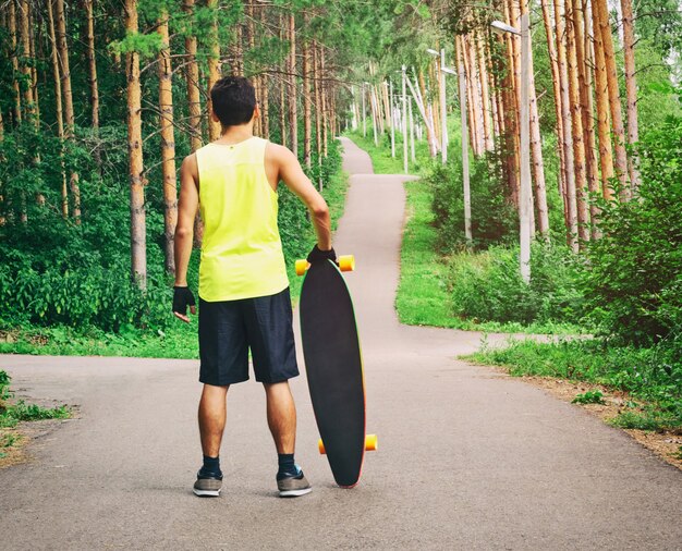 Achter mening van jonge kerel die met longboard of skateboard op de weg klaar om in park te schaatsen blijft