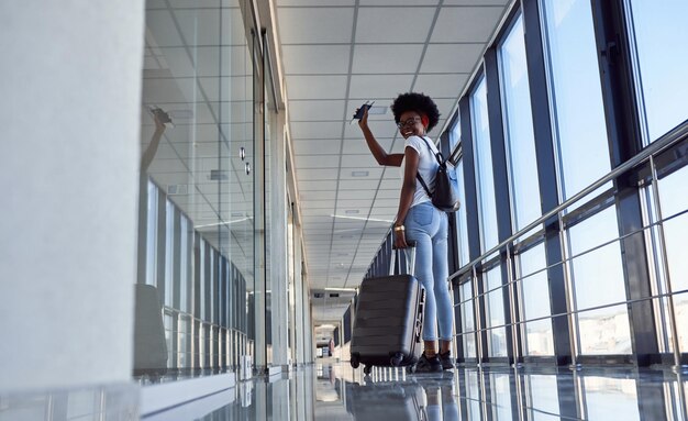 Achteraanzicht als jonge Afro-Amerikaanse vrouwelijke passagier in vrijetijdskleding op de luchthaven met bagage.