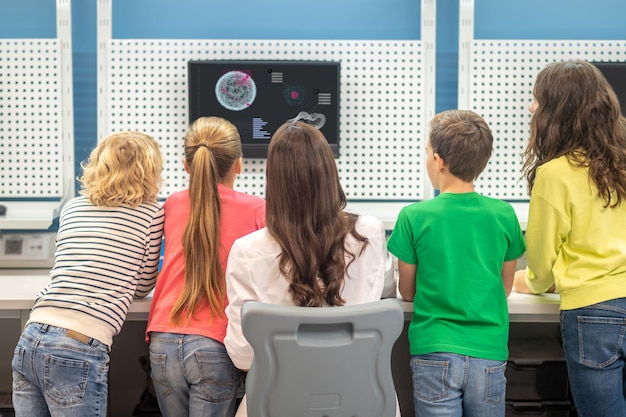 Achteraanzicht bij leraar met kinderen die naar de monitor kijken