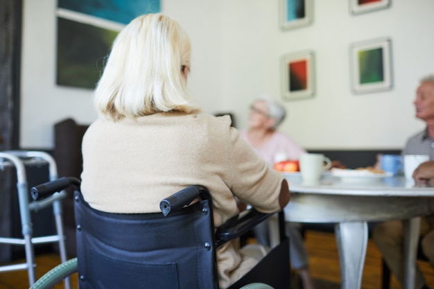 Achteraanzicht bij witharige oudere vrouw die in een rolstoel zit in de kopieerruimte van het verpleeghuis