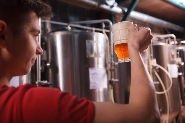 Achteraanzicht bijgesneden opname van een mannelijke brouwer die bierglas vasthoudt en de kwaliteit van een drank onderzoekt