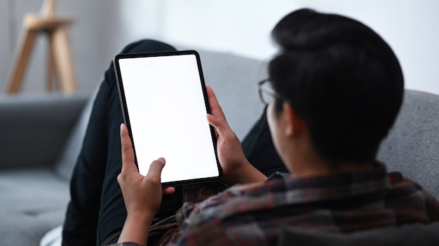 Achteraanzicht casual man zittend op de bank en met behulp van digitale tablet.