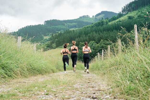 Achteraanzicht drie mooie vrouwen rennen over een weg door een bos