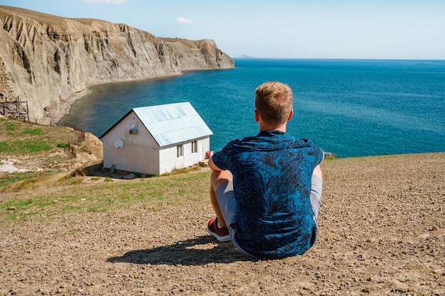 Achteraanzicht een jonge man voor een wit eenzaam huis aan de rand van een klif