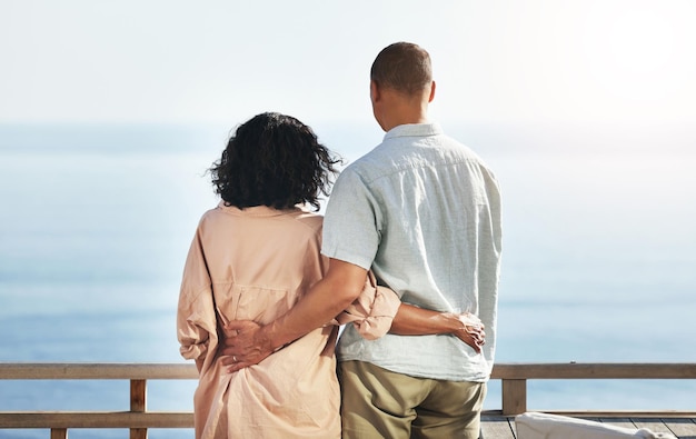 Achteraanzicht en senior paar bij strandknuffel en genieten van quality time op vakantie of vakantie Liefdeszorg en gepensioneerde oudere man en vrouw knuffelen omhelzen of knuffelen terwijl ze plezier hebben bij oceaan of zee