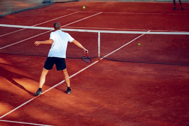 Achteraanzicht foto van een man tennissen op de tennisbaan