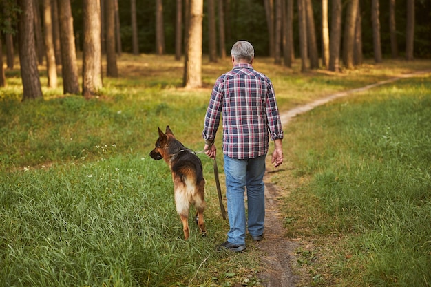 Achteraanzicht foto van een ouder wordende man en zijn hond wandelen in het bos