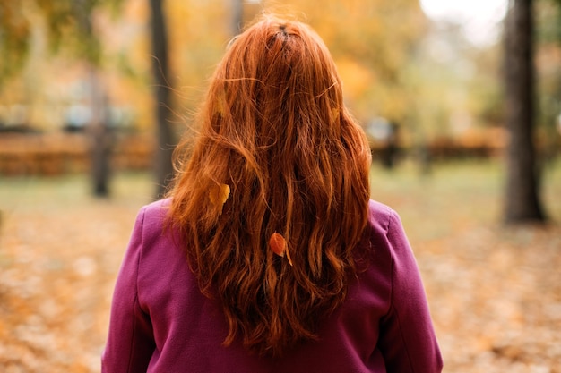 Achteraanzicht gezichtsloos portret van roodharig meisje met herfstbladeren in haar herfstportret van happy