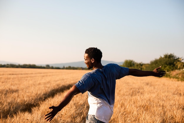 Achteraanzicht jonge boer die in het midden van het veld staat met rijpe tarwe Afro-Amerikaanse man die tarweaartjes aanraakt Slow living concept