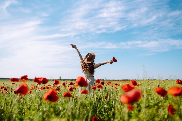 Achteraanzicht Jonge gekrulde vrouw in hoed poseren in het papaverveld Zomerlandschap