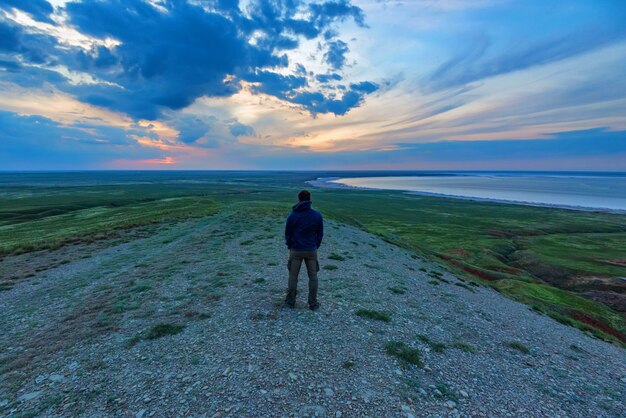 Foto achteraanzicht jonge mannelijke wandelaar kijkt naar zee en horizon