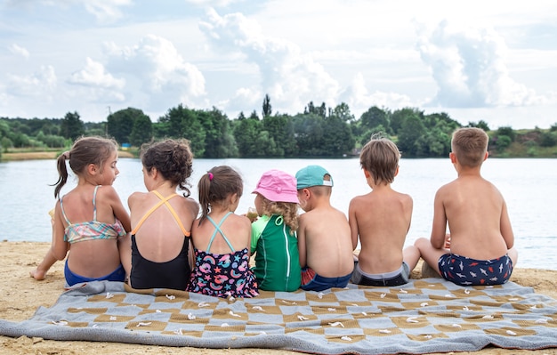 Achteraanzicht kinderen zitten bij de rivier en ontspannen na het zwemmen, zonnebaden, ijs eten.