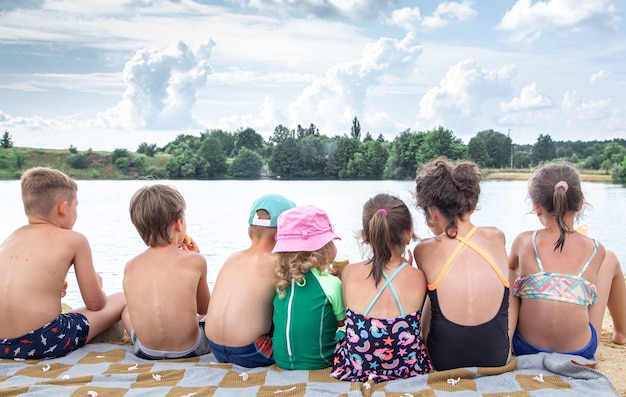 Achteraanzicht kinderen zitten bij de rivier en ontspannen na het zwemmen, zonnebaden, ijs eten.