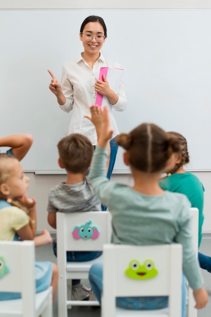 Foto achteraanzicht leerling die een vraag wil beantwoorden tijdens de les