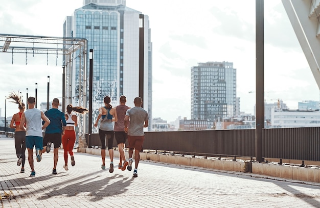 Achteraanzicht over de volledige lengte van mensen in sportkleding die joggen terwijl ze buiten op het trottoir trainen
